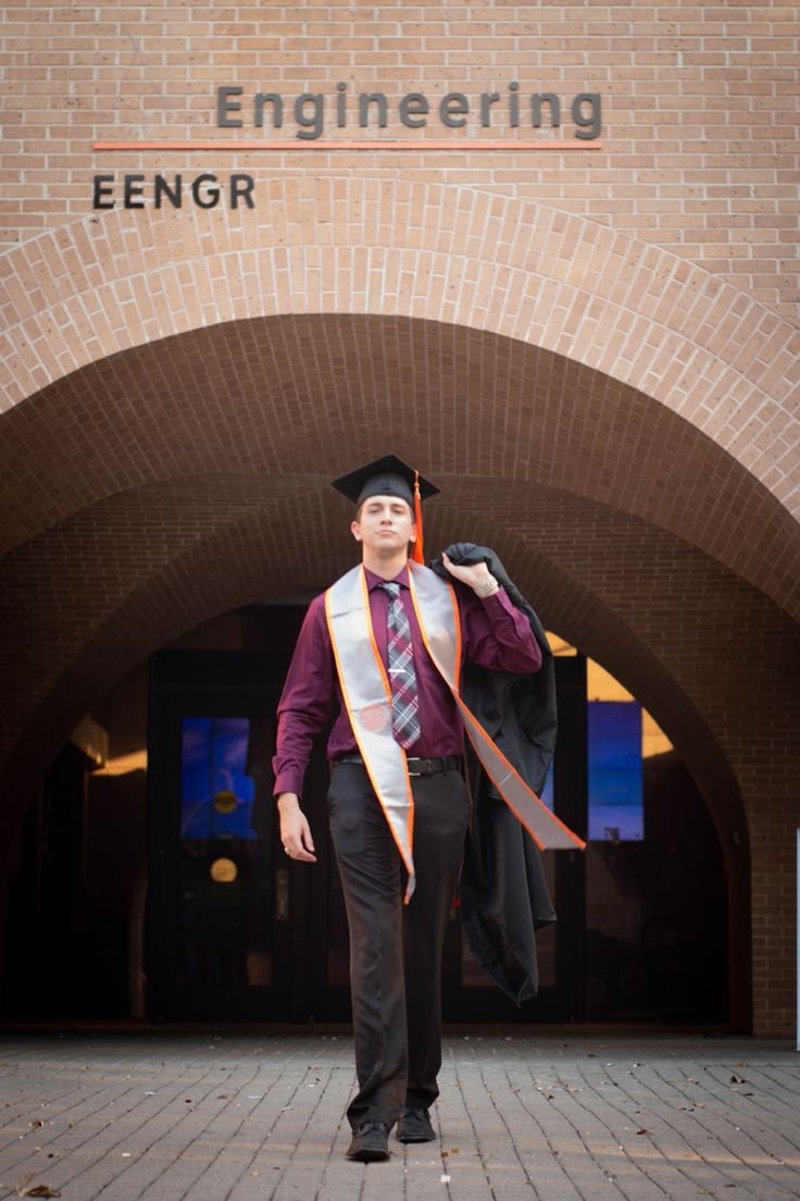 a man in a graduation cap and gown is standing outside an engineering building with his diploma