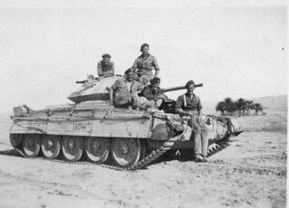 men sitting on top of a tank in the desert