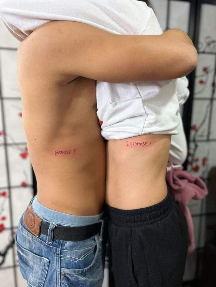 two people with small tattoos on their backs, one is holding the other's back