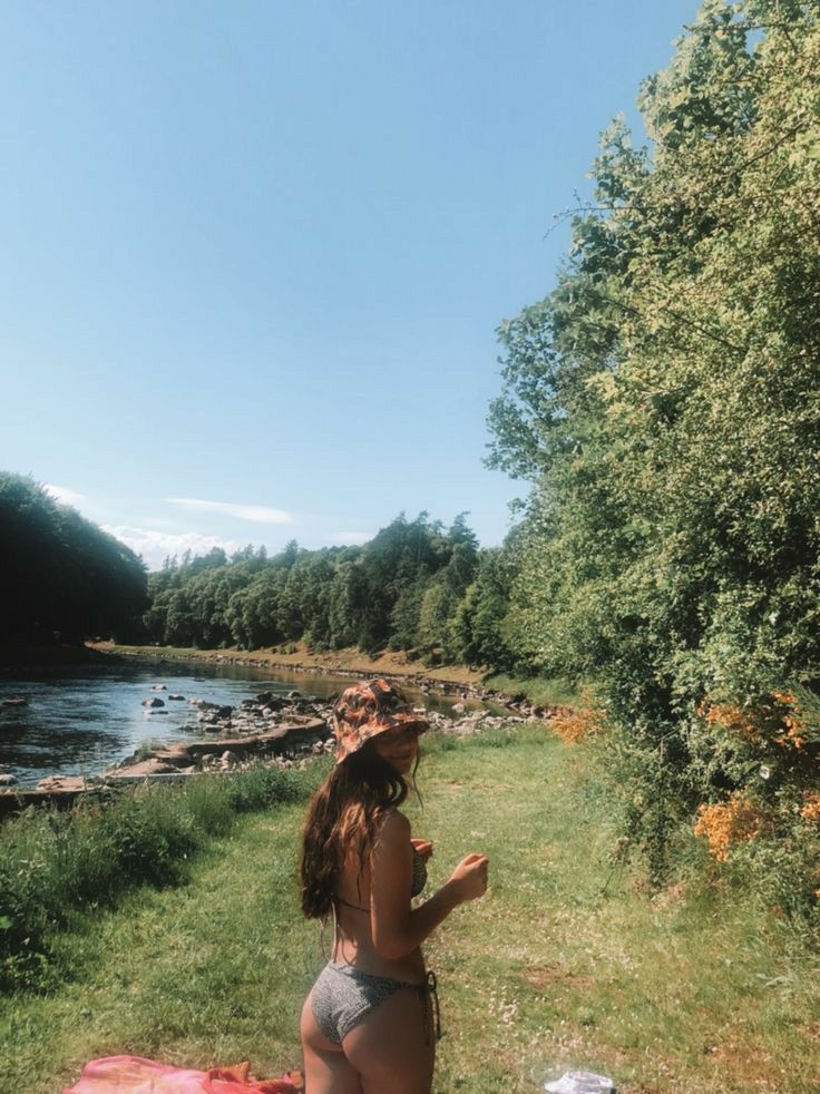 a woman in a bathing suit sitting on a blanket by the edge of a river