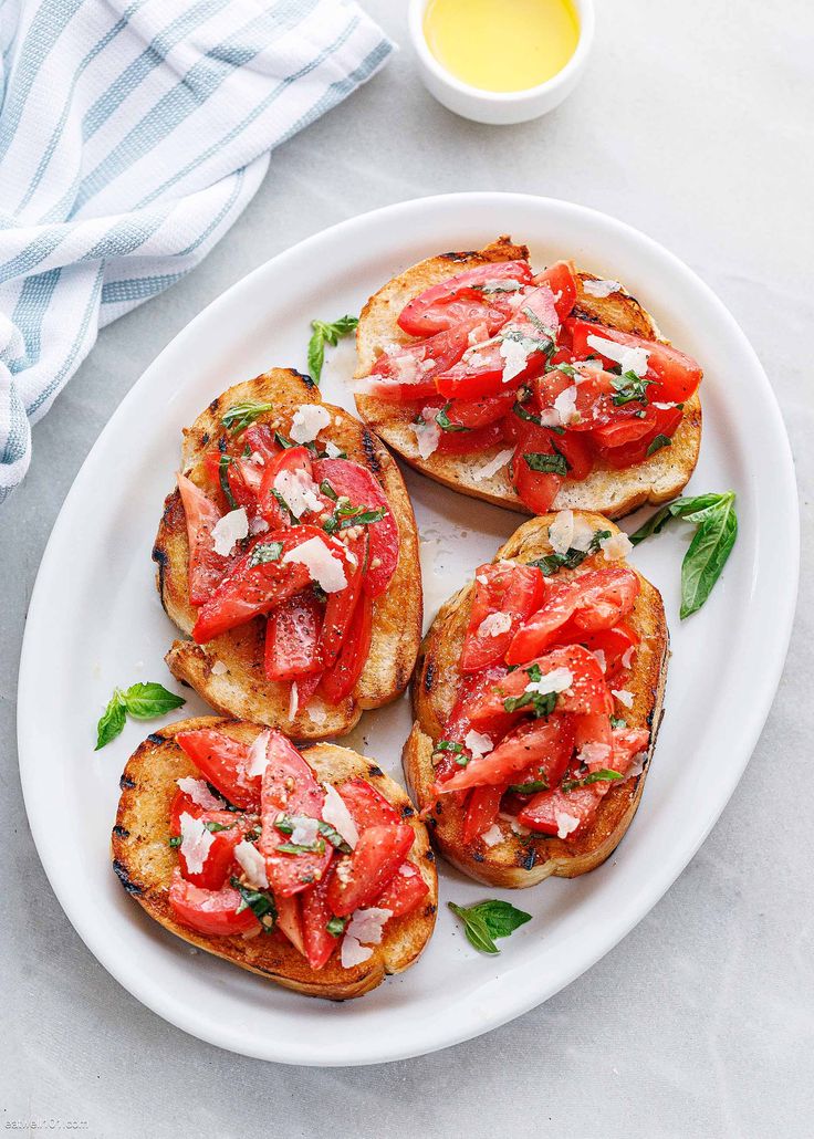 four pieces of bread with tomatoes and cheese on them sitting on a white plate next to a cup of mustard