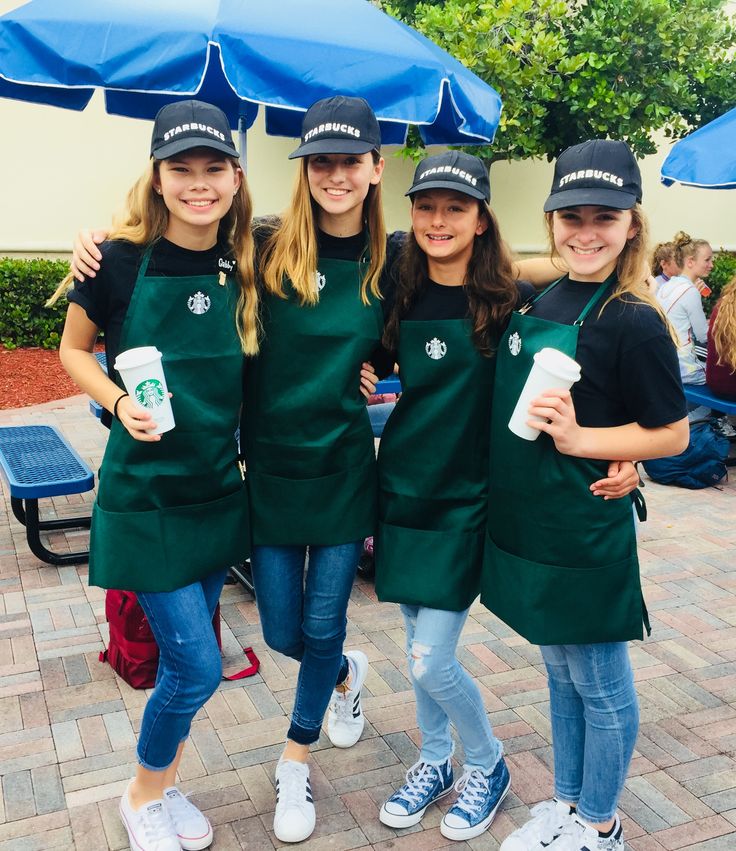 three girls in green aprons and hats under an umbrella