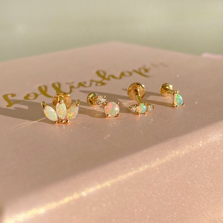 three pairs of opalite studs sitting on top of a pink box with gold lettering