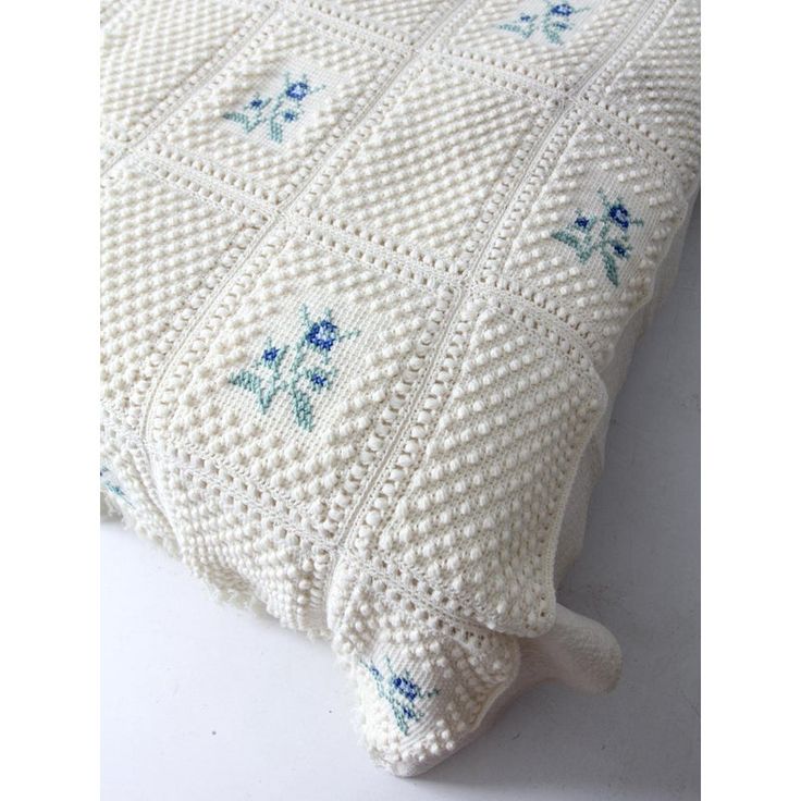 a white crocheted pillow with blue flowers on it's sides and the bottom