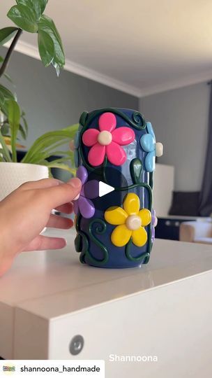 a person holding a flower shaped object on top of a table next to a potted plant