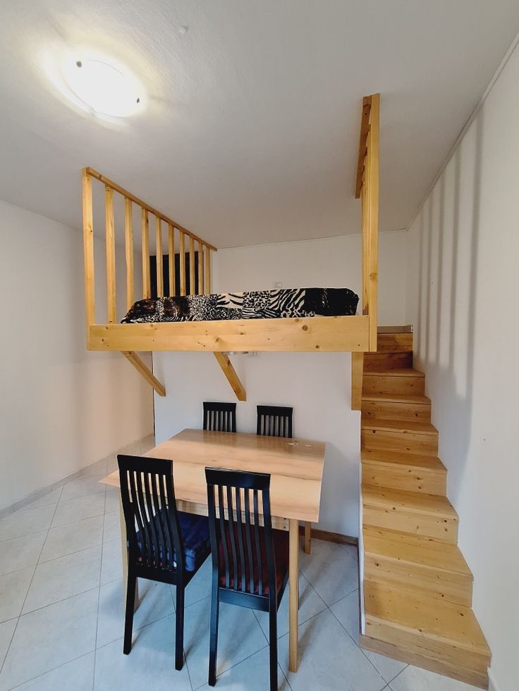 there is a table and chairs in the room with stairs to the loft bed above