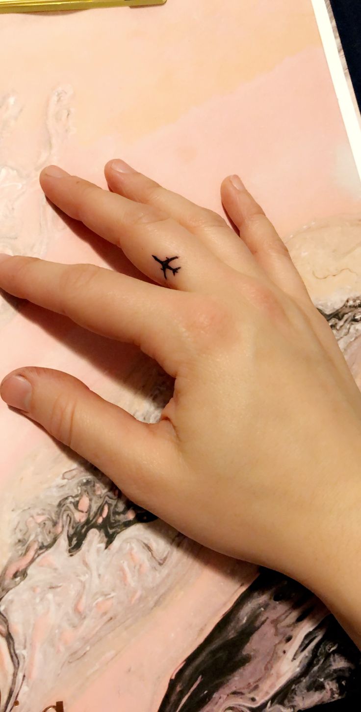 a woman's hand with a tiny black bird tattoo on her left index finger