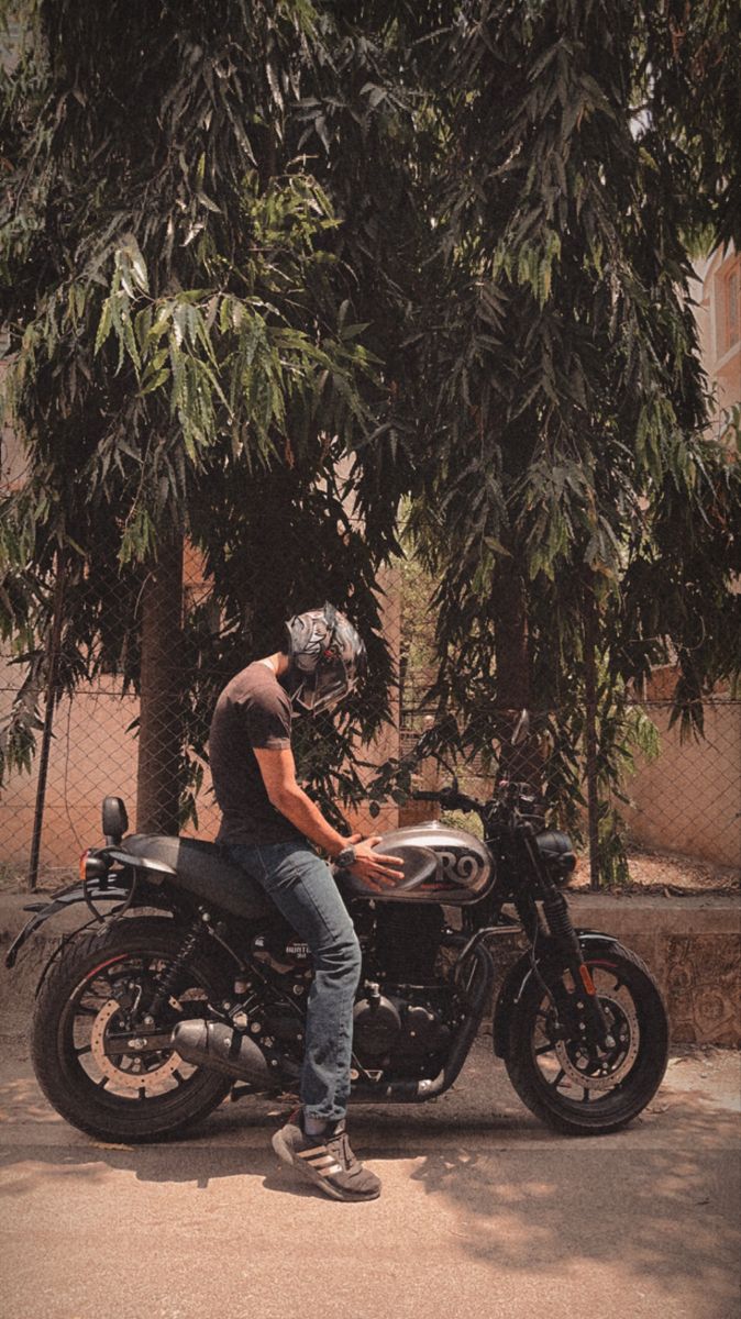 a man riding on the back of a motorcycle down a street next to a tree