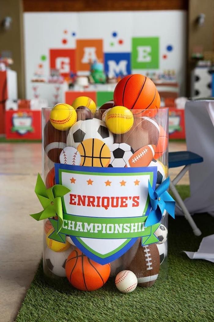 a plastic bucket filled with sports balls on top of a green carpeted floor next to a chair