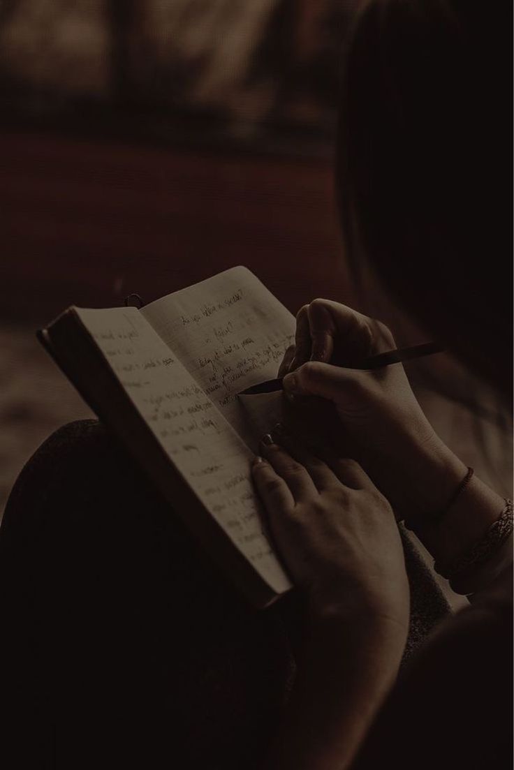 a woman is writing on a notebook in the dark with her hand holding a pen