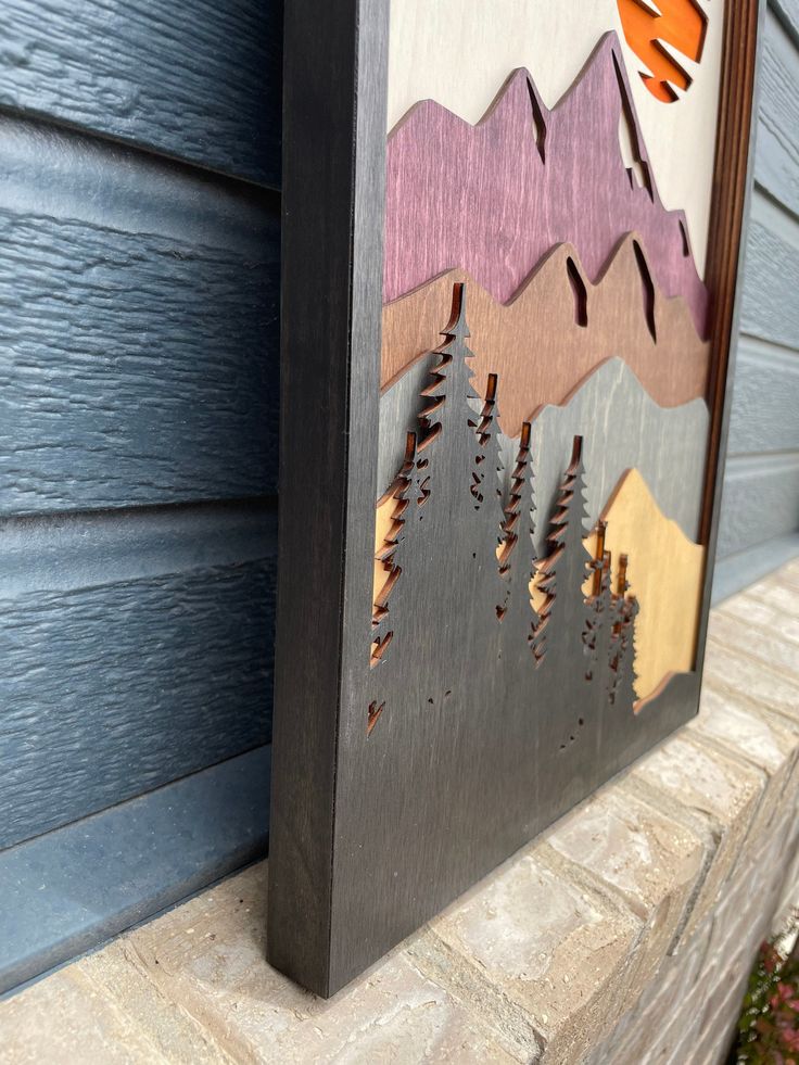 a wooden sign with mountains and trees painted on the side of a blue house,