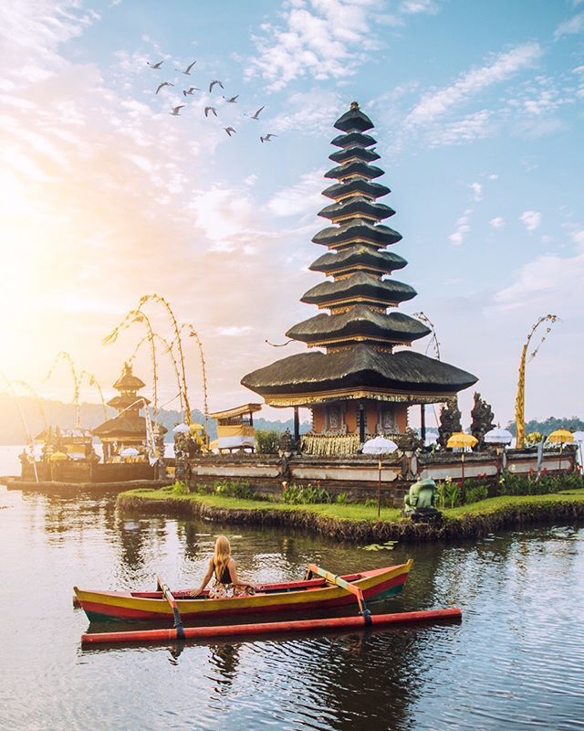 a woman in a canoe on the water with a pagoda in the background and birds flying overhead