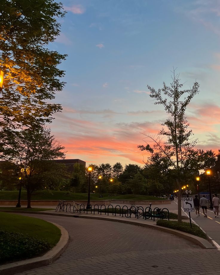 the sun is setting over a park with people walking around