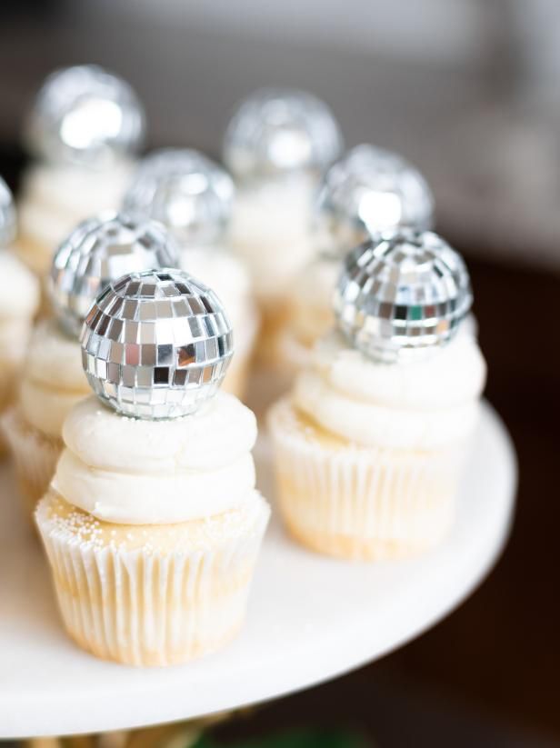 cupcakes with white frosting and silver decorations on a cake platter,