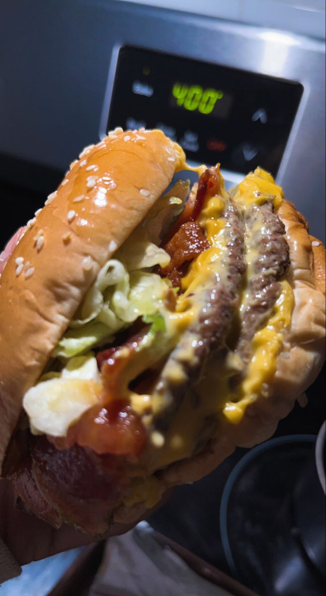 a hand holding a hot dog with cheese, bacon and lettuce on it