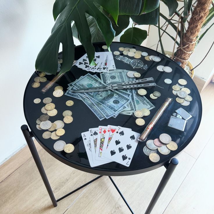 a black table topped with lots of money and playing cards next to a potted plant