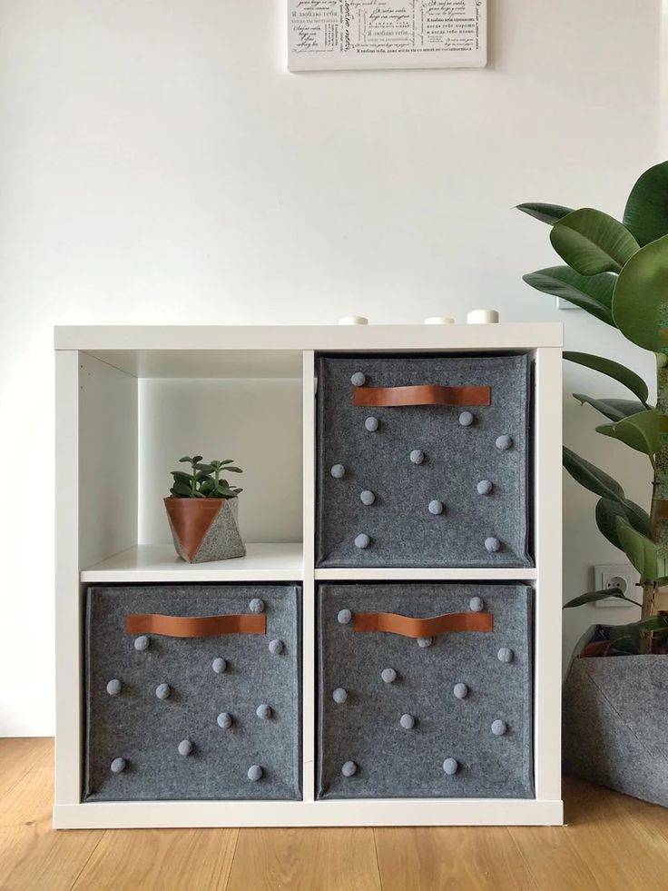 a white shelf with four baskets on top of it next to a potted plant