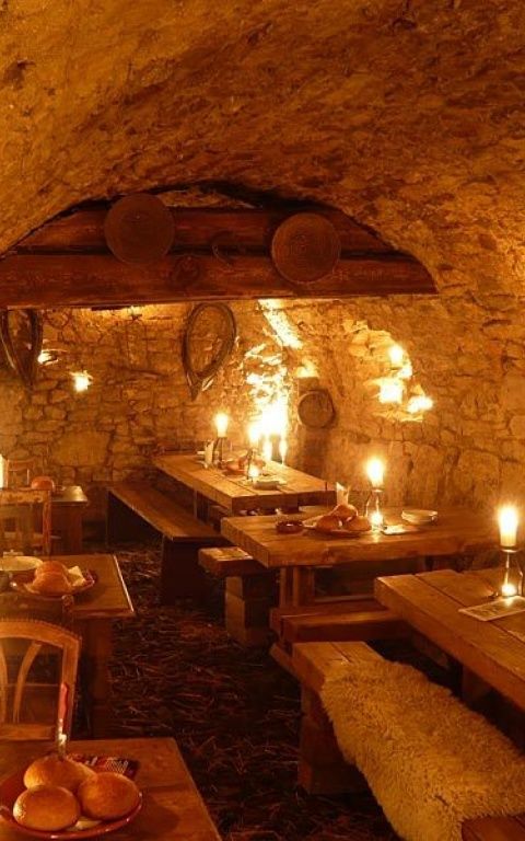 an old stone restaurant with candles lit up in the middle and wooden tables on either side