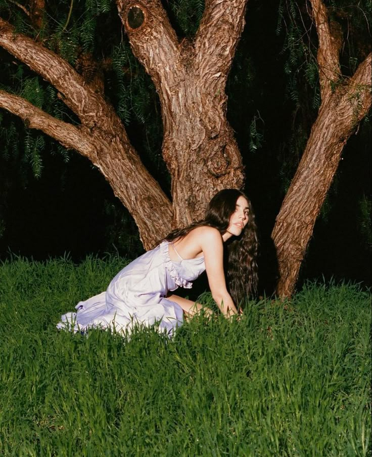 a woman sitting in the grass next to a tree