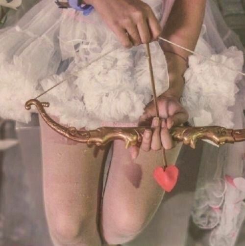 a woman in white dress holding a bow and arrow with red heart on it's string