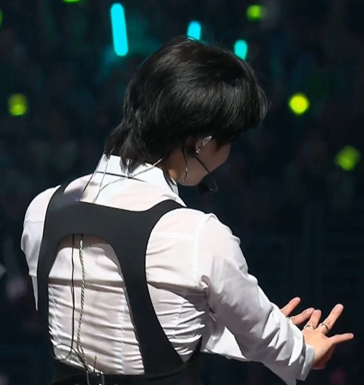 a man with black hair wearing suspenders and holding his hands out