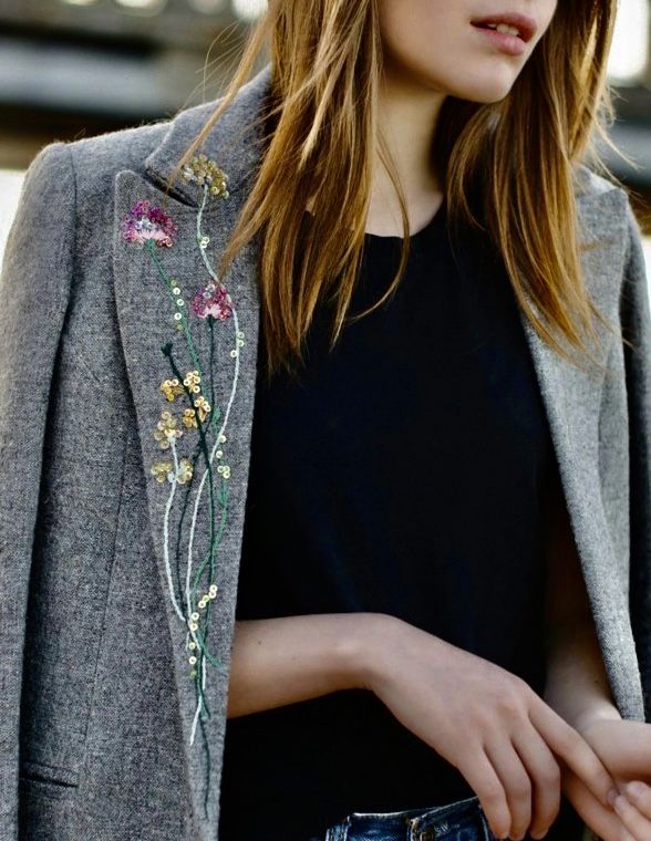 a woman in black shirt and grey blazer with flower embroidered on the back pocket