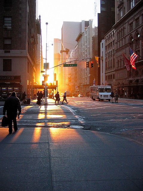 people crossing the street at sunset on a busy city street