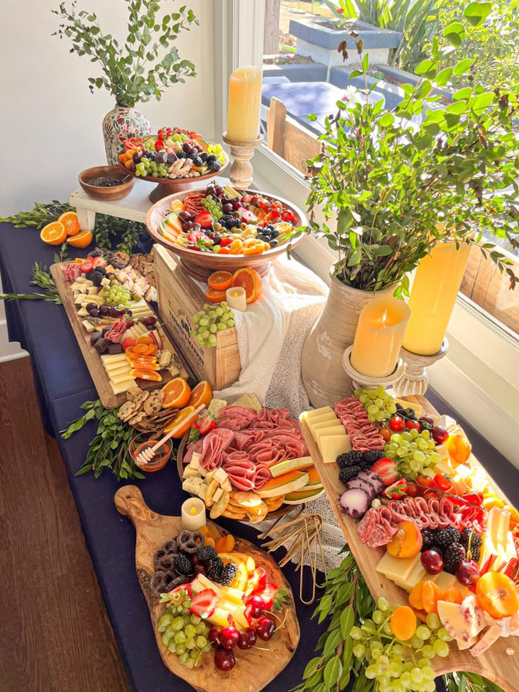 an assortment of meats, cheeses and vegetables on a table in front of a window