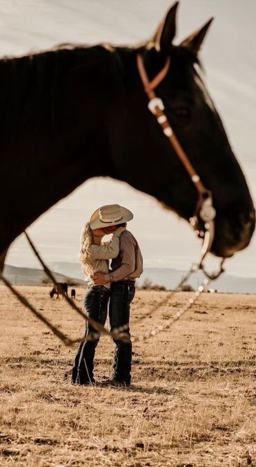 a man standing next to a horse in the middle of a field with his hat on