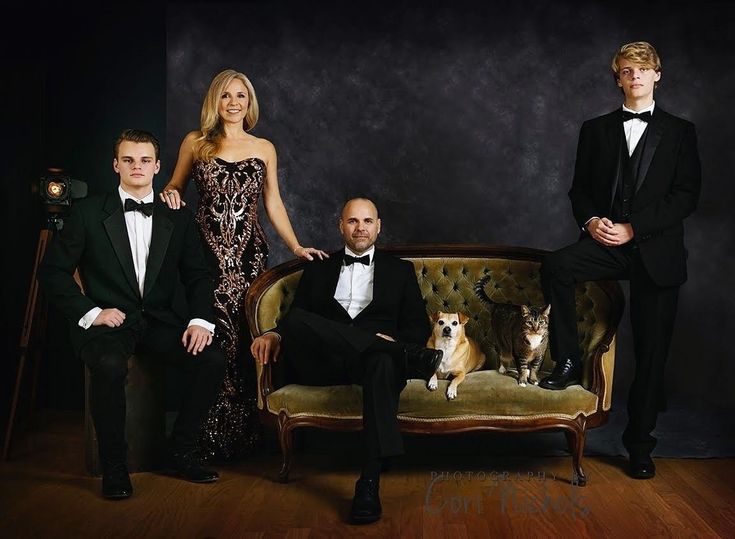 three people and a dog sitting on a couch in front of a black wall with a dark background