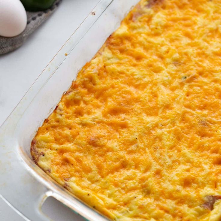 an egg casserole in a glass dish on a table with eggs and utensils