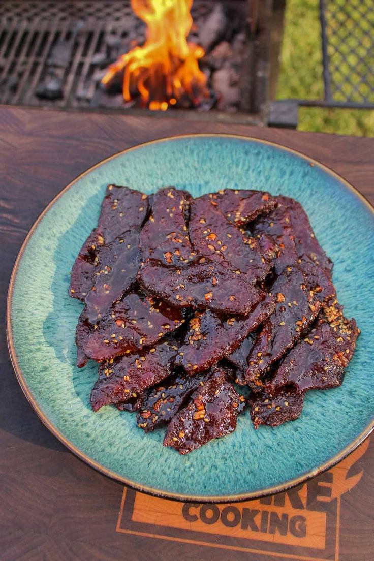 a blue plate topped with meat next to a fire