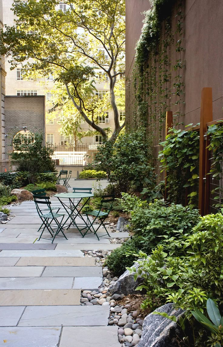 an outdoor patio with tables and chairs surrounded by greenery on either side of the building