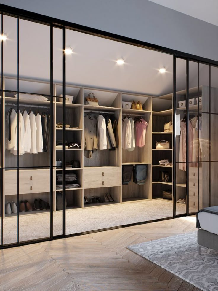 an open closet with clothes and shoes on the shelves next to a bed in a bedroom