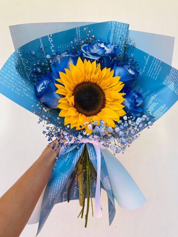 a sunflower is being held by someone's hand with blue ribbon and flowers