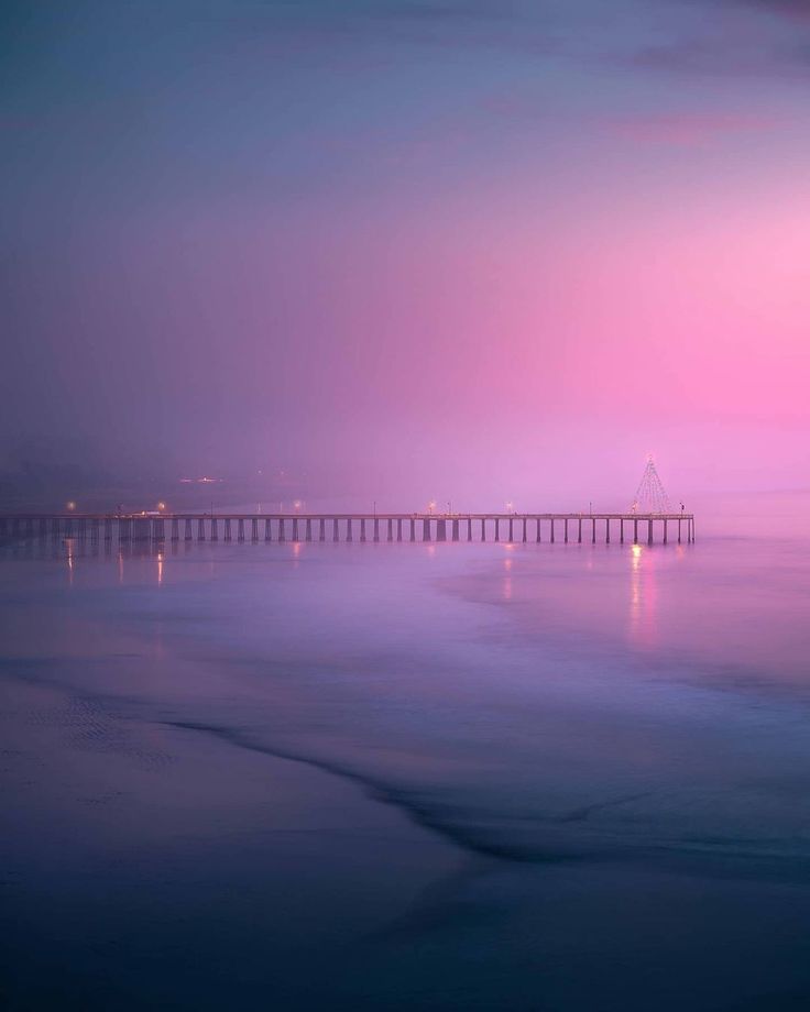 a long bridge that is over the ocean at night with pink and blue sky in the background