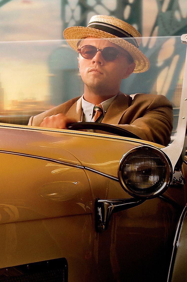 a man in a suit and hat sitting in an old car