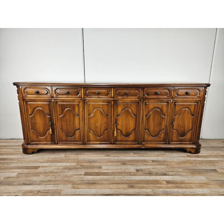 an old wooden sideboard with carvings on the doors and drawers is shown against a white wall