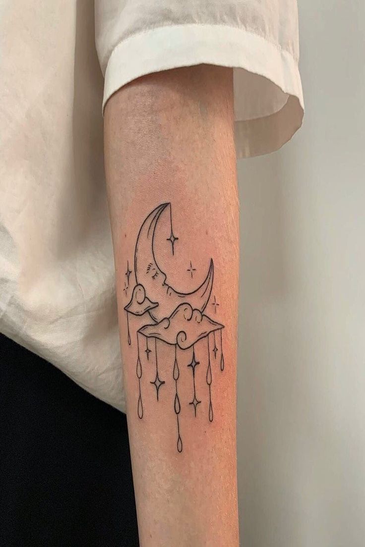 a person with a tattoo on their arm that has a crescent moon and stars hanging from it