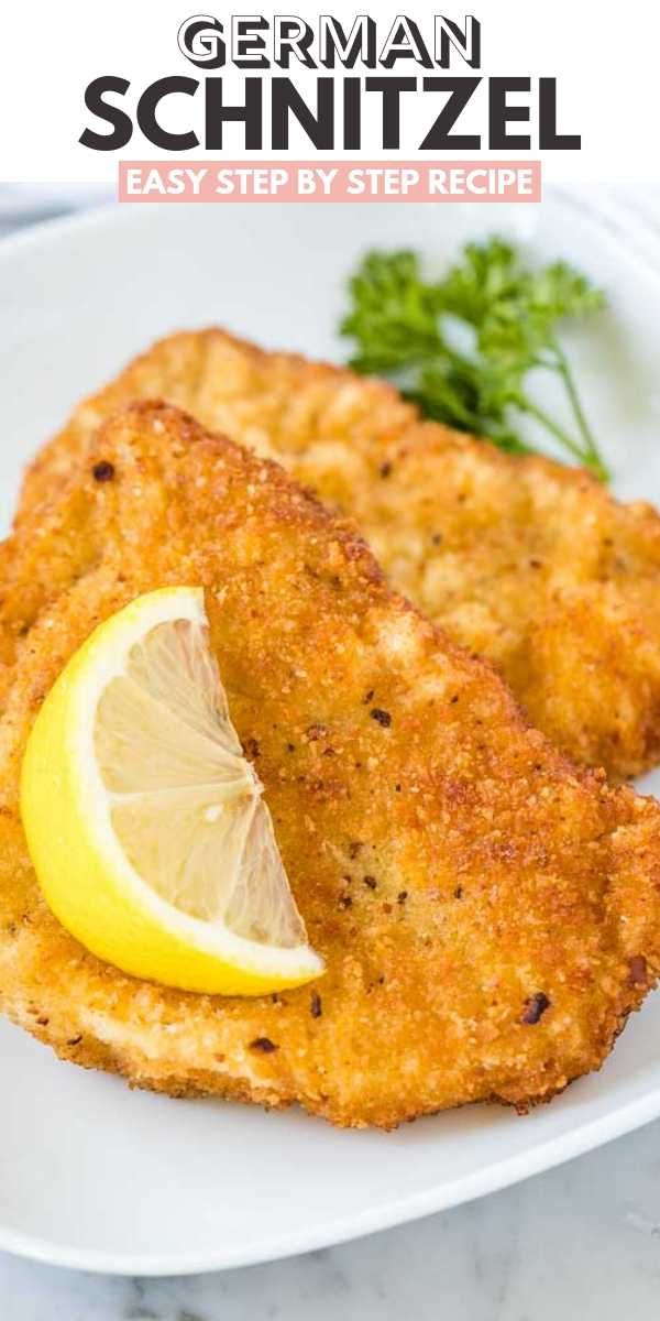 two pieces of fried fish on a white plate with lemon wedges and parsley