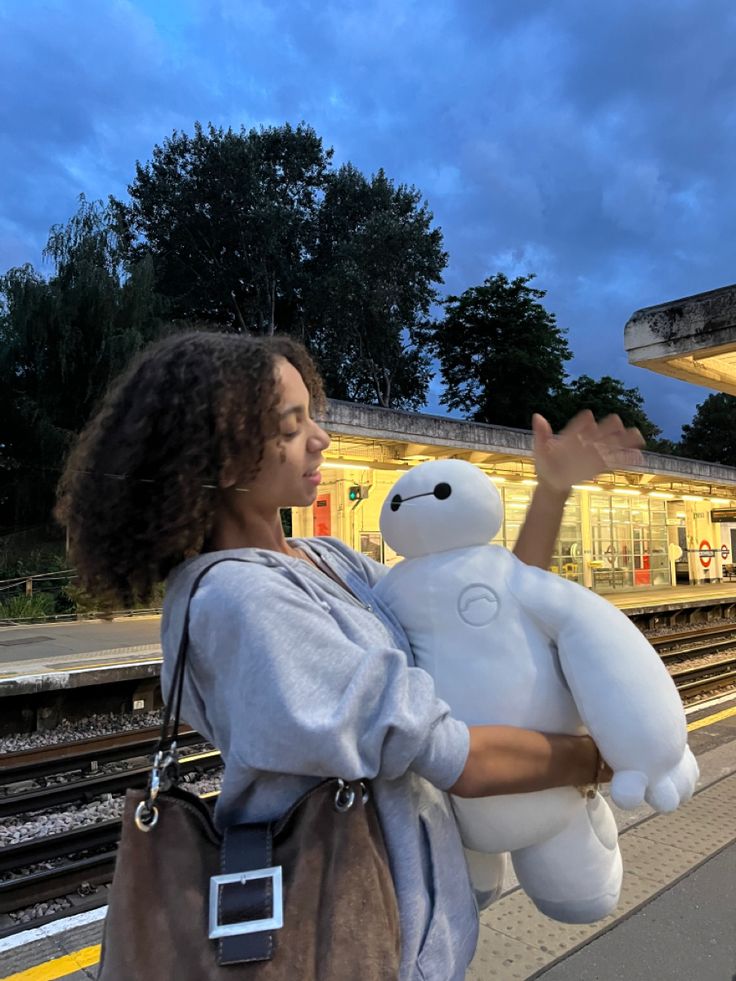 a woman holding a large white teddy bear in front of a train station at night