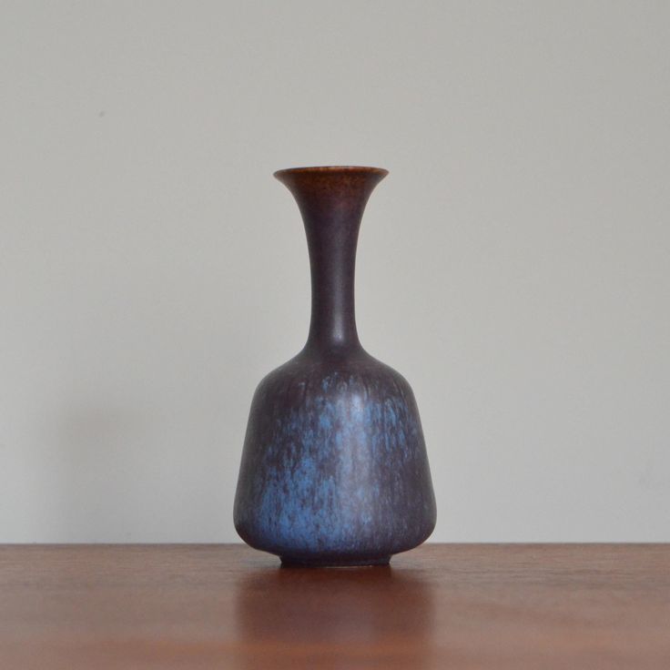 a brown vase sitting on top of a wooden table next to a white wall in the background