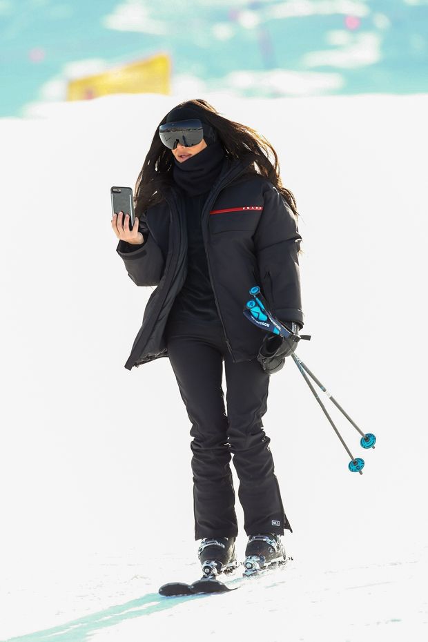 a woman walking in the snow with skis and holding a cell phone to her ear