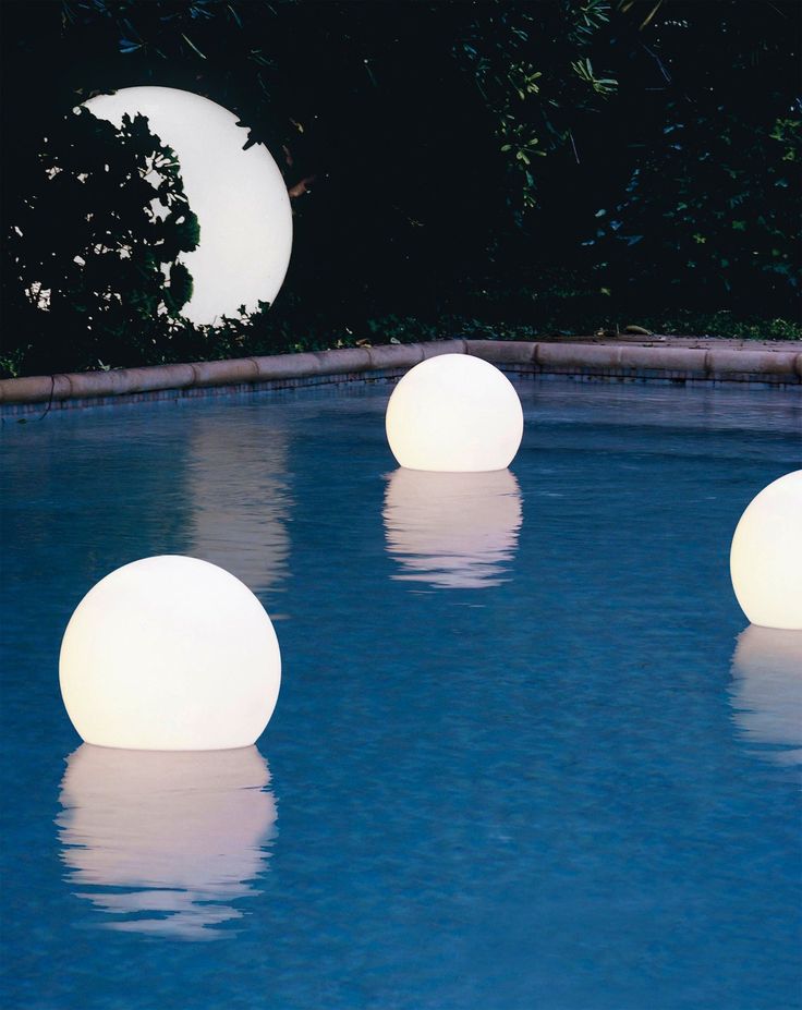 three white balls floating on top of a swimming pool next to trees and moon in the sky