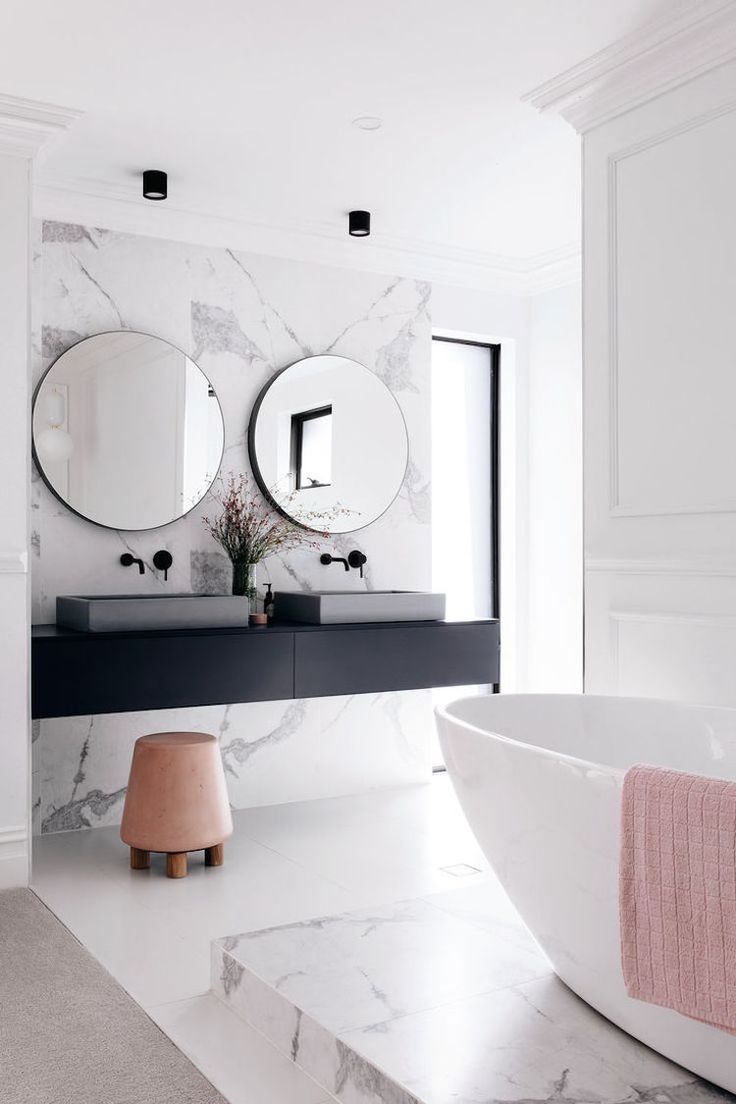 a bathroom with marble walls and flooring, two round mirrors on the wall above the sink