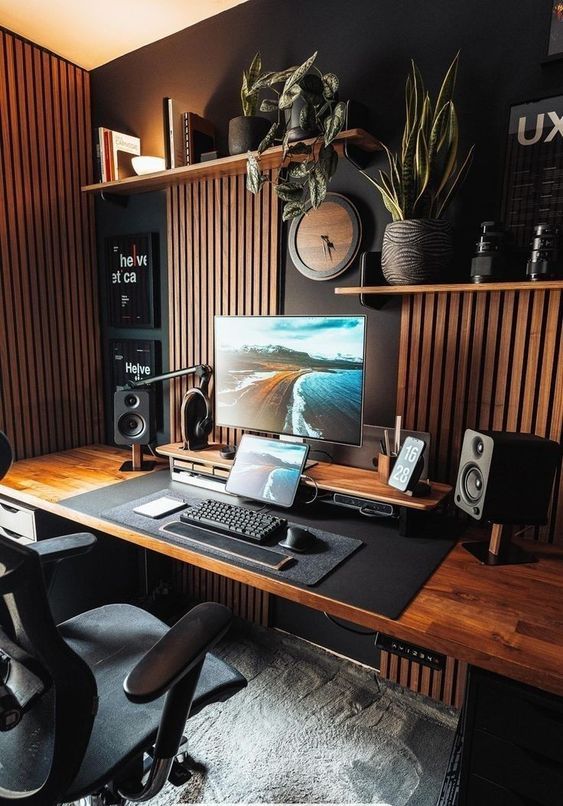 a desk with a computer and speakers on it in front of a wooden paneled wall