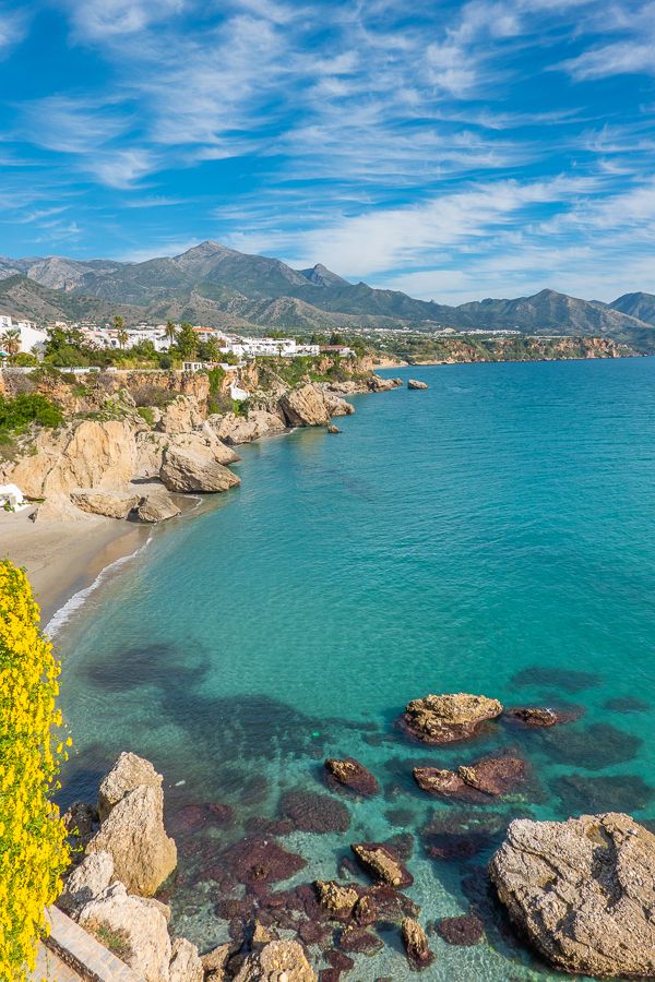 the beach is surrounded by rocks and water with yellow flowers growing on it's shore