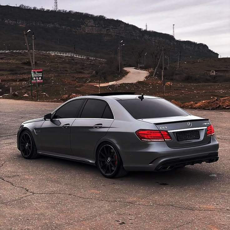 a grey car parked on top of a parking lot next to a hill and road