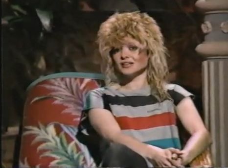 a woman sitting on top of a chair in front of a plant and wearing a striped shirt