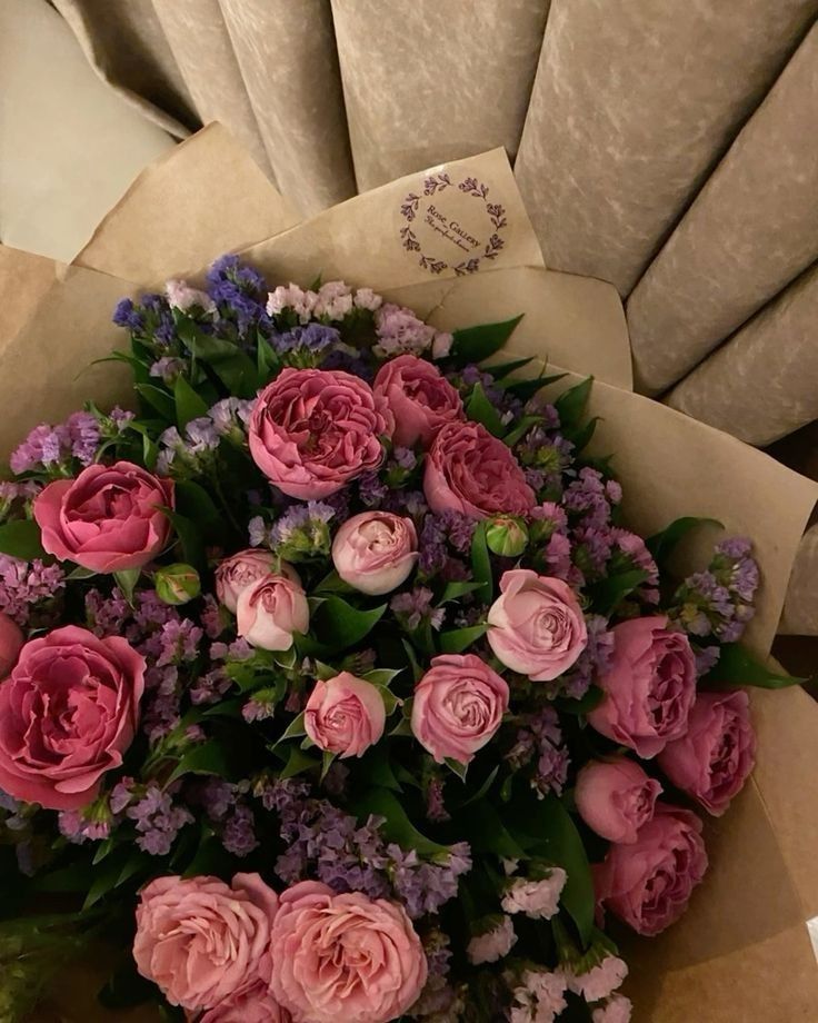 a bouquet of pink and purple flowers sitting on top of a table next to a pillow